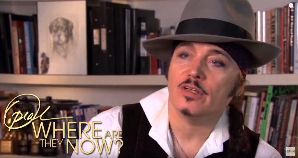 Screen capture of Adam Ant on Oprah's Television show "Where are they now?" with Artist Chelsea Smith's Original pencil pet portrait of his dog she created for him hanging up in his house in the background