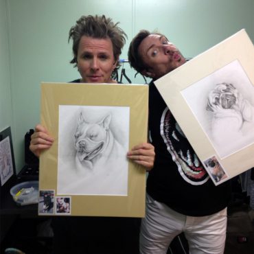 John Taylor (Bassist) on the left and Simon Le Bon (singer) on the right from Duran Duran holding up original pencil pet portraits of their dogs created by Artist Chelsea Smith