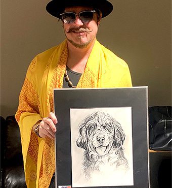Scott Holiday lead guitarist for the band Rival Sons holding up a original pencil pet portrait of his dog gypsy by Artist Chelsea Smith